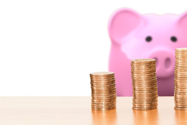 Alcancía de cerdo rosa mirando hacia pilas de monedas que están en primer plano