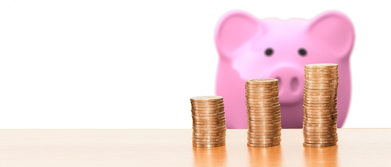 Alcancía de cerdo rosa mirando hacia pilas de monedas que están en primer plano
