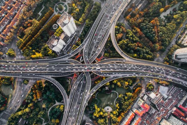 Fotografía tomada desde la altura a un distribuidor vial, donde se aprecian coches circulando, parques y edificios.